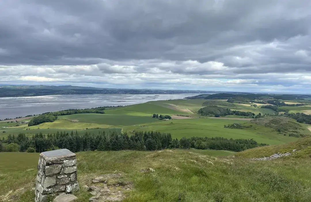 Scenic view of a landscape with a stone monument, grassy fields, and a body of water under a cloudy sky.